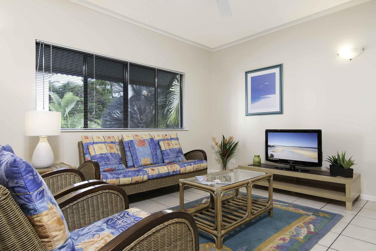 A living room with a sofa, chairs, a coffee table, a television, and a window with blinds.