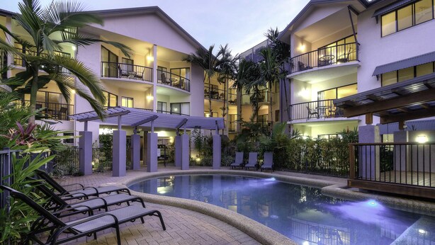 A hotel courtyard with a swimming pool, lounge chairs, and multiple balconies with outdoor seating. - Bay Villas Resort (Port Douglas)