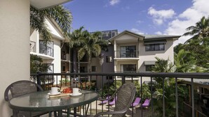 A balcony with a glass table, chairs, and a view of neighboring buildings and palm trees. - Bay Villas Resort (Port Douglas)