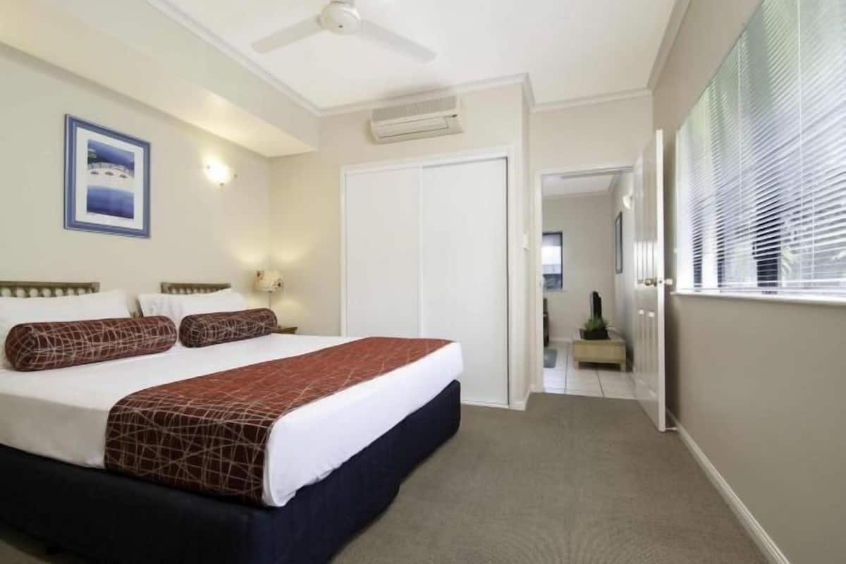 A hotel room with a bed, a ceiling fan, an air conditioning unit, a door, and a window with blinds.