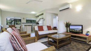 A living room with wicker furniture, a television, and a kitchen in the background. - Bay Villas Resort (Port Douglas)