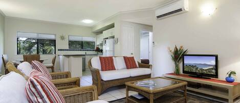 A living room with wicker furniture, a television, and a kitchen in the background.