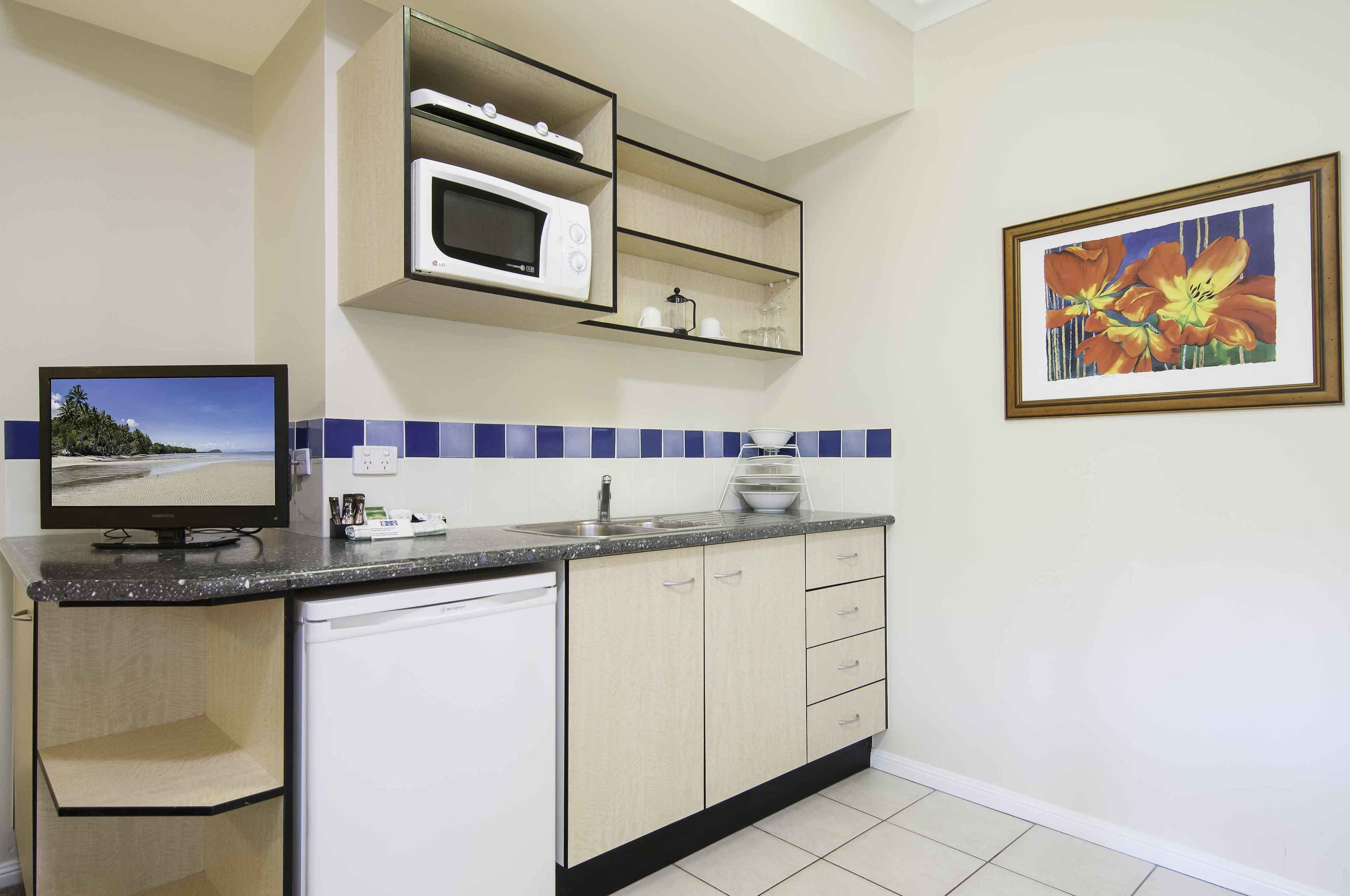 A compact kitchen with a microwave, a sink, and a dishwasher. There is a television on the counter and a framed picture on the wall.