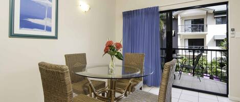 A dining area with a glass table surrounded by wicker chairs, a vase with flowers, and a framed picture on the wall.