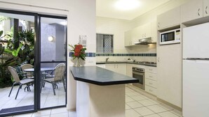 A kitchen with a central island, white cabinets, a microwave, and an oven. - Bay Villas Resort (Port Douglas)
