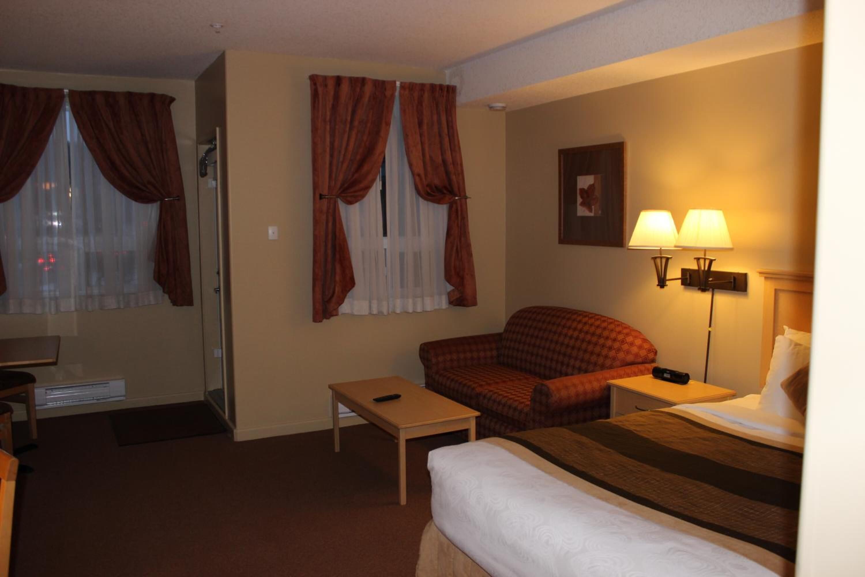 A hotel room with a bed, a desk, a chair, a sofa, and a lamp.