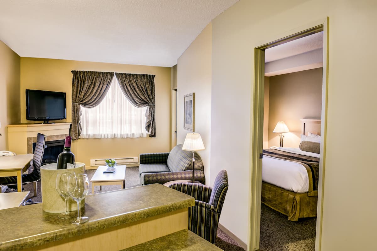 A hotel room with a bed, a sofa, a small table, a TV, a lamp, and a wine glass.