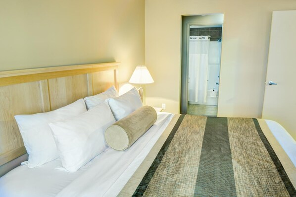 A hotel room with a bed, a nightstand, a lamp, and a bathroom door.