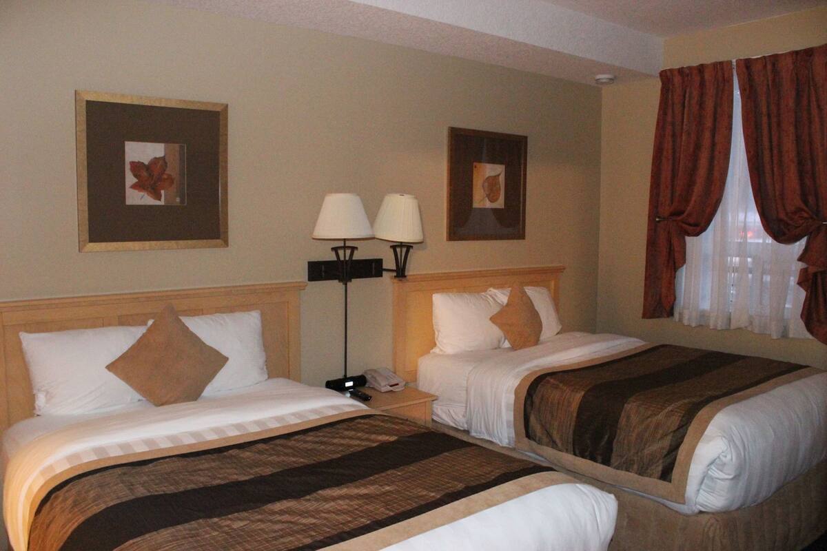 A hotel room with two beds, a nightstand with a lamp, and framed pictures on the wall.