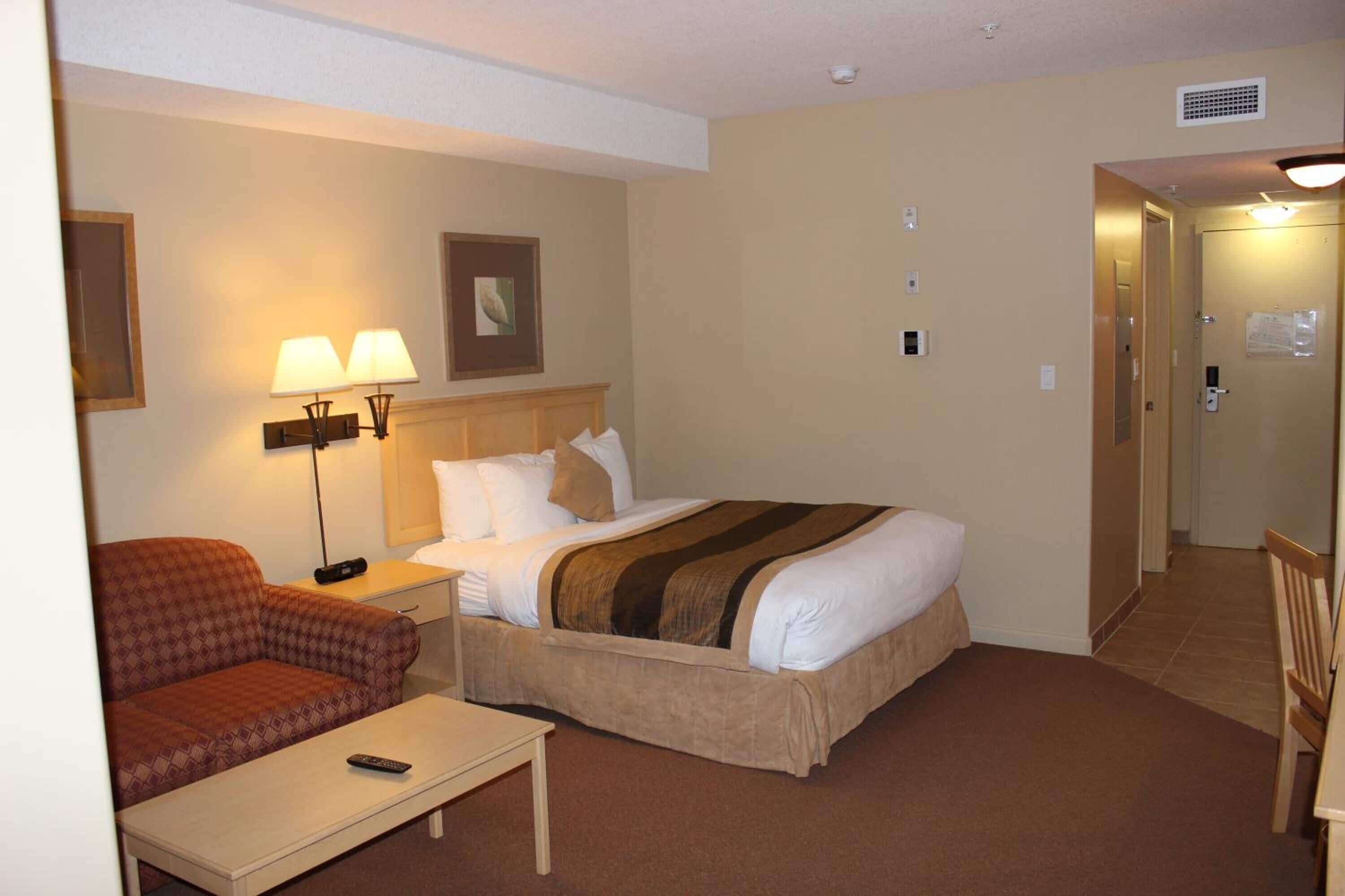 A hotel room with a bed, a chair, a desk, a lamp, and a picture on the wall.