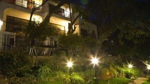 Un edificio de varios pisos con balcones, rodeado de un jardín bien iluminado durante la noche.