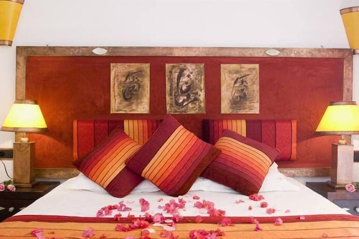 A bed with a wooden headboard, two bedside lamps, and three framed artworks above the bed.