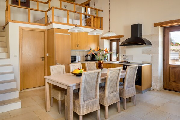 A modern kitchen with wooden cabinets, a dining table with wicker chairs, and a black range hood.