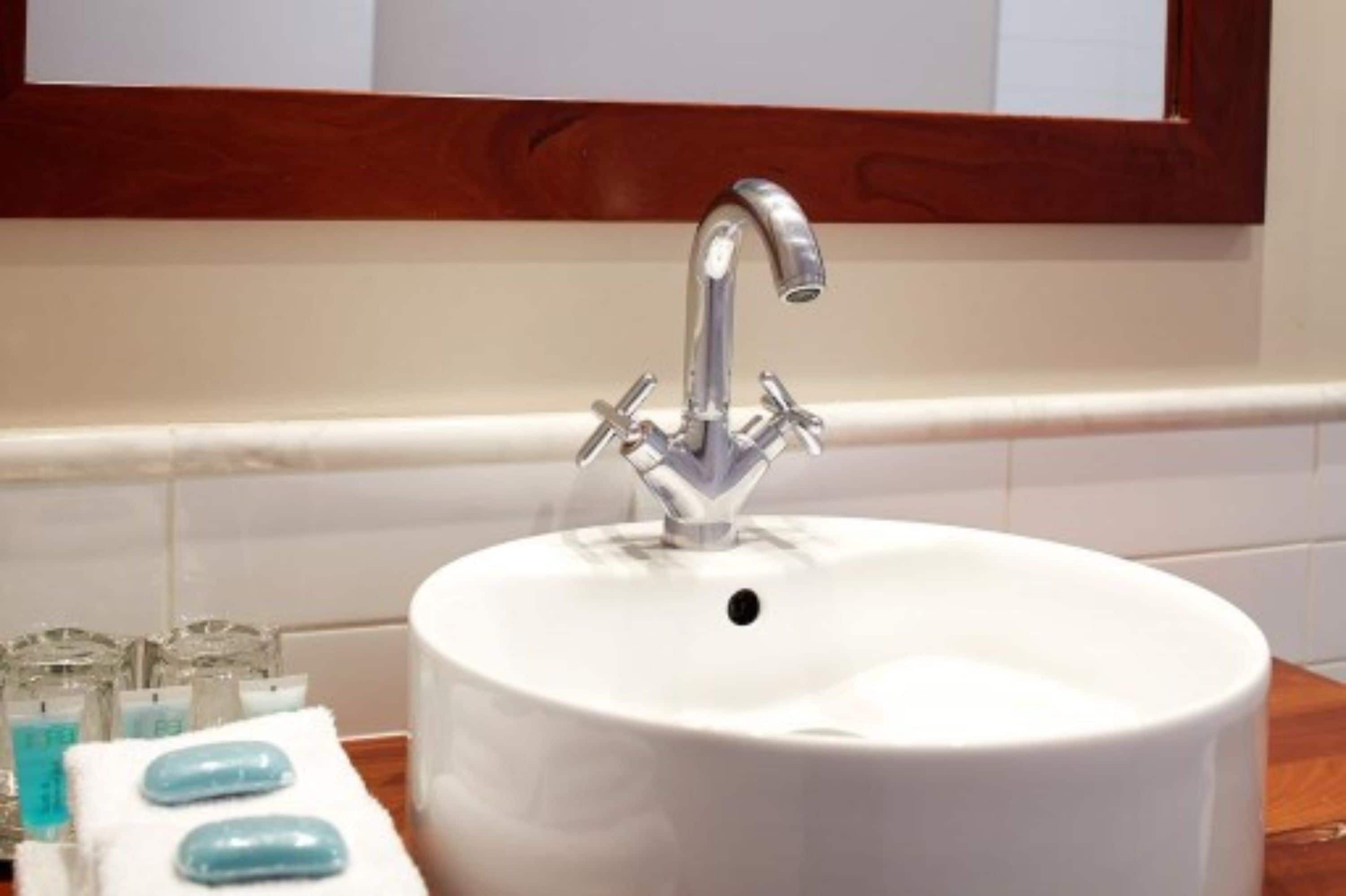 Un lavabo de salle de bain doté d’un robinet moderne, un miroir au-dessus et un plan de toilette blanc avec du savon et une serviette.