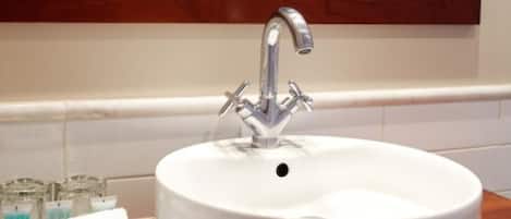 Un lavabo de salle de bain doté d’un robinet moderne, un miroir au-dessus et un plan de toilette blanc avec du savon et une serviette.