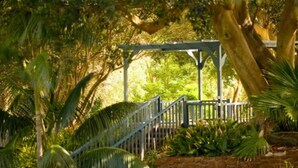 A garden with a wooden pergola, stone pathway, and various tropical plants. - Seashells Yallingup (Yallingup)