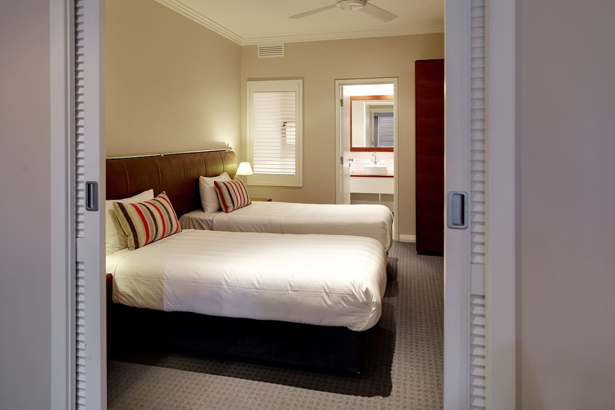 Habitación de hotel con dos camas, baño con espejo y ventilador de techo.