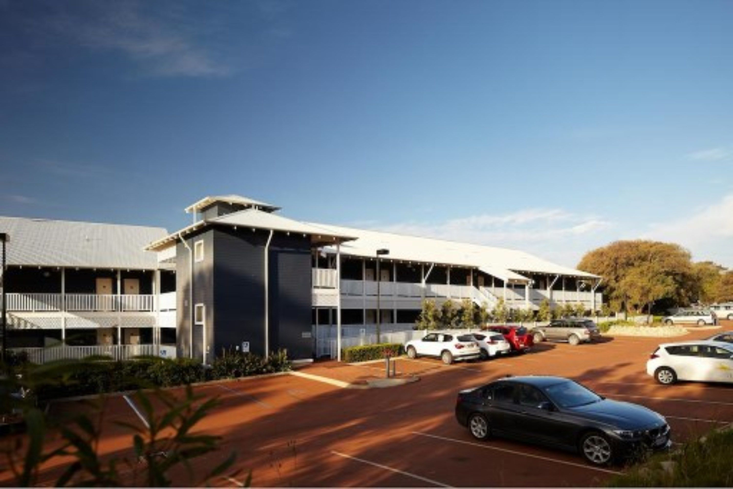A modern building with a flat roof, a covered parking area, and a few cars parked in front.