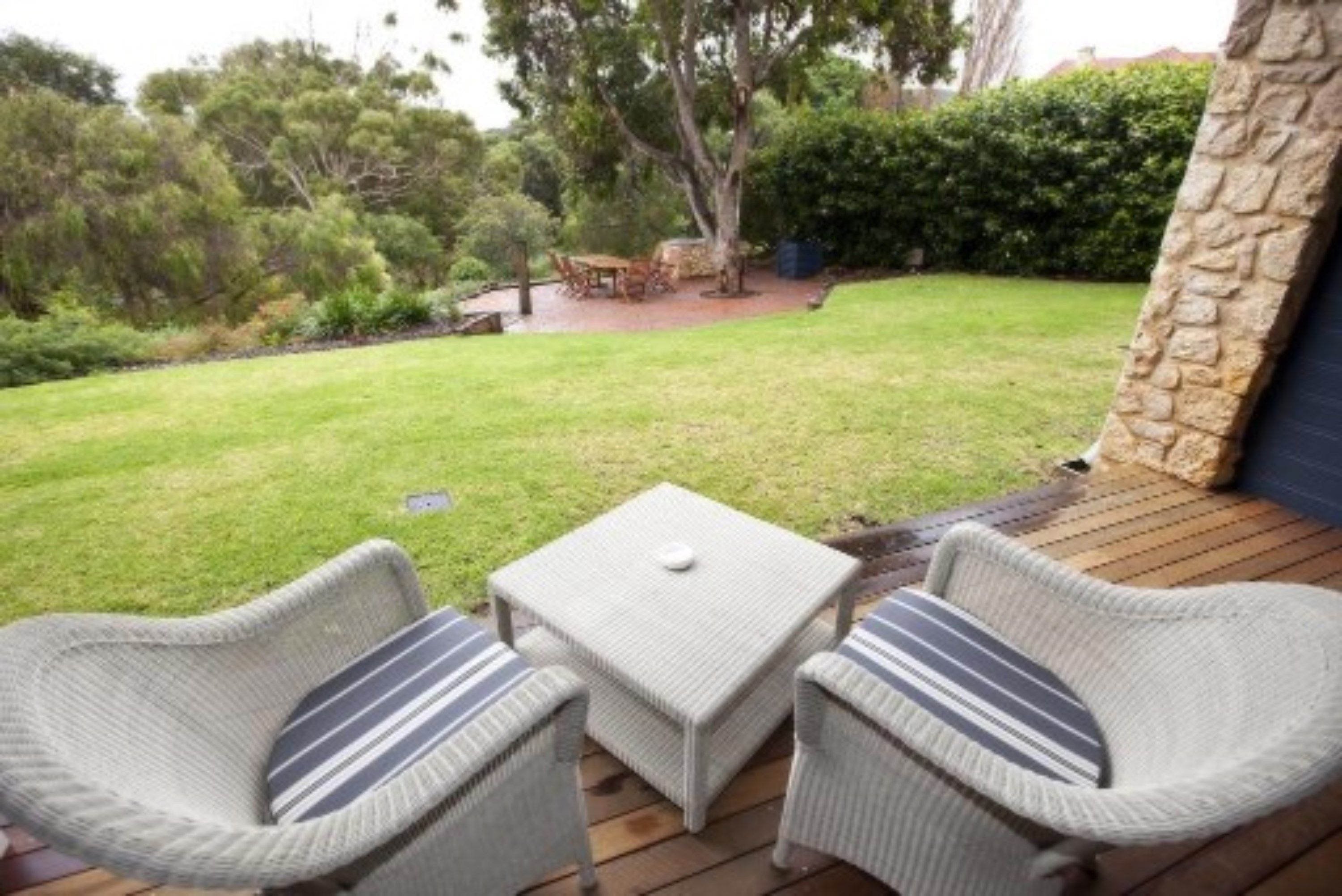 A patio with wicker furniture and a small table, surrounded by a grassy lawn and trees.