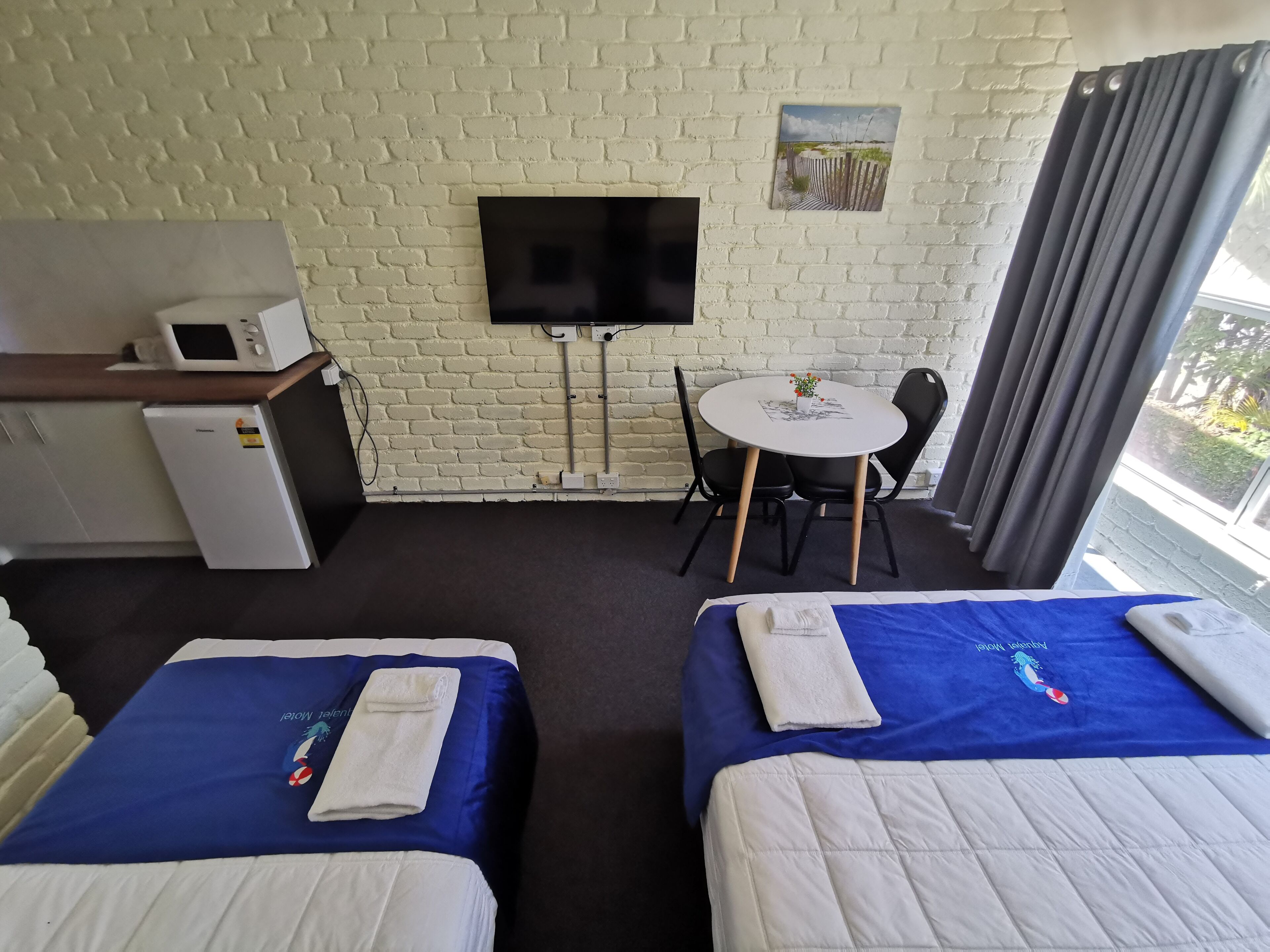 Une chambre d’hôtel avec deux lits, un bureau équipé d’un micro-ondes, une télévision et une petite table avec des chaises.