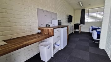 A compact room with a kitchenette, a flat-screen TV, and a bed with a blue blanket.
