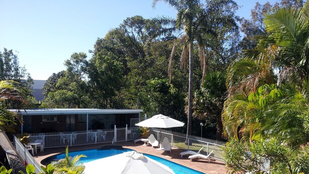 Piscina rodeada de exuberante vegetación, con zona de estar cubierta y terraza cercada.