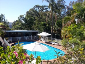 A swimming pool surrounded by lush greenery, with a covered seating area and a fenced deck. - Aquajet Motel (Coffs Harbour)