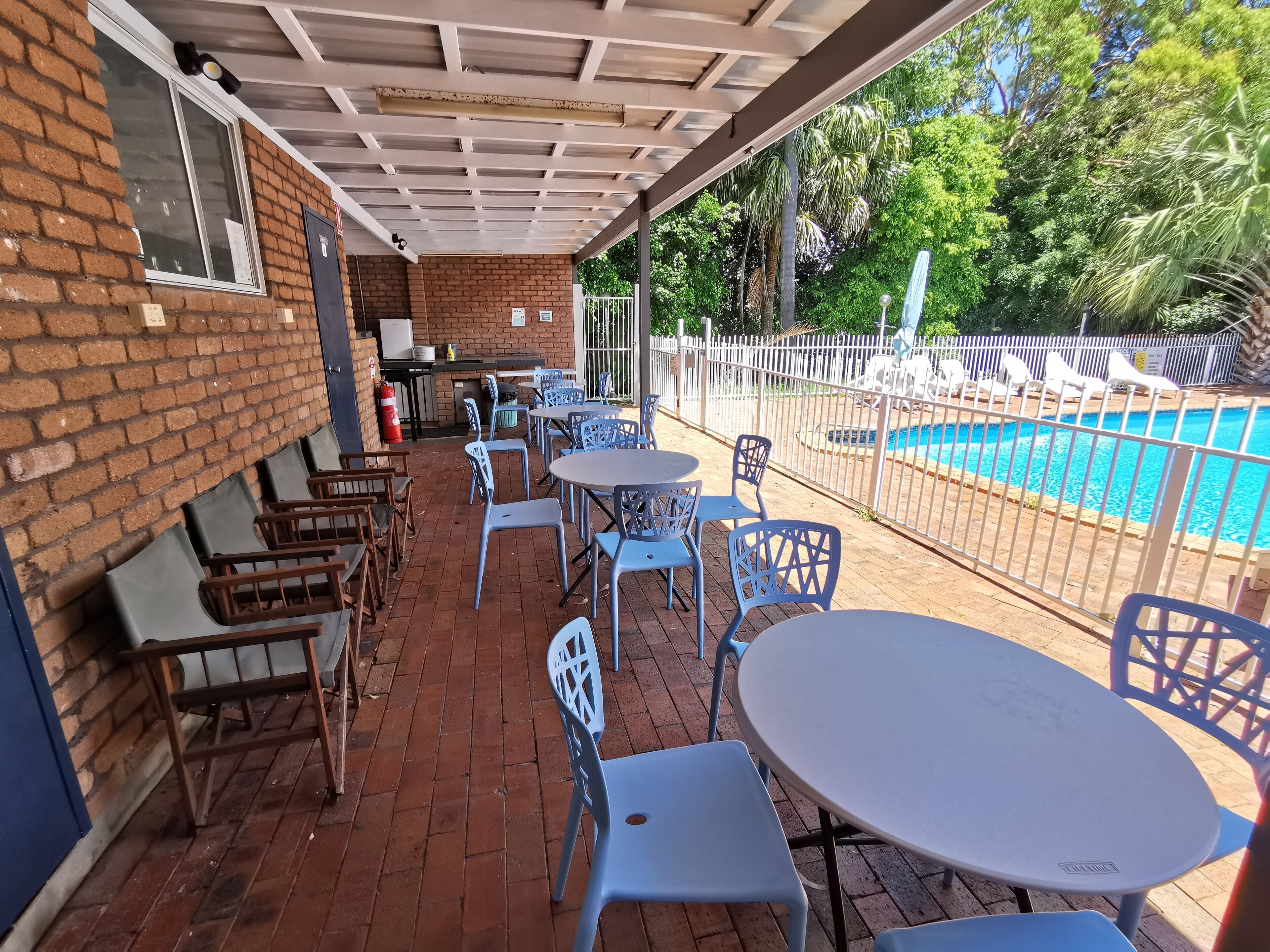 A covered patio area with brick flooring, outdoor seating, and a view of a swimming pool.