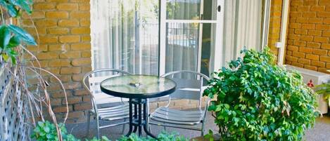 A patio with a table and chairs, a brick wall, and a potted plant.