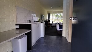 Cocina compacta con microondas, un lavamanos pequeño y un cubo de basura. Hay una ventana que proporciona luz natural y vistas al exterior.