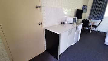 A compact room with a kitchenette, a small dining table with two chairs, and a window with curtains.
