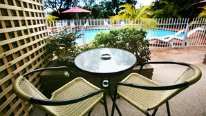 Un patio con una mesa redonda y dos sillas de mimbre, una piscina y una valla blanca.