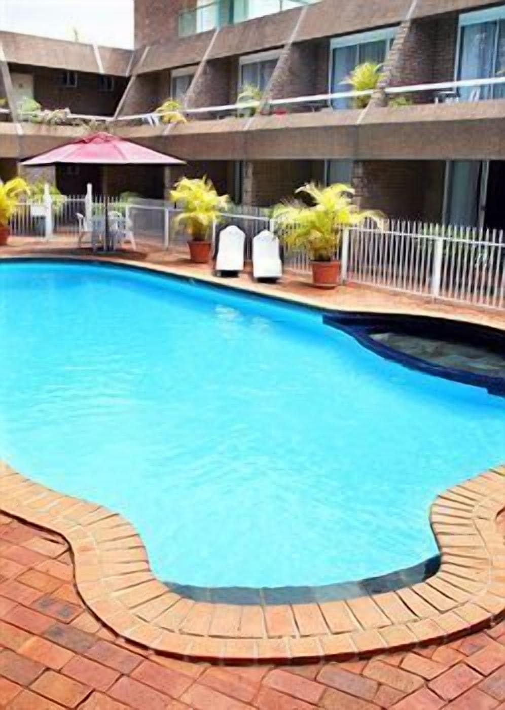 A swimming pool with a brick border, surrounded by potted plants and a white fence.