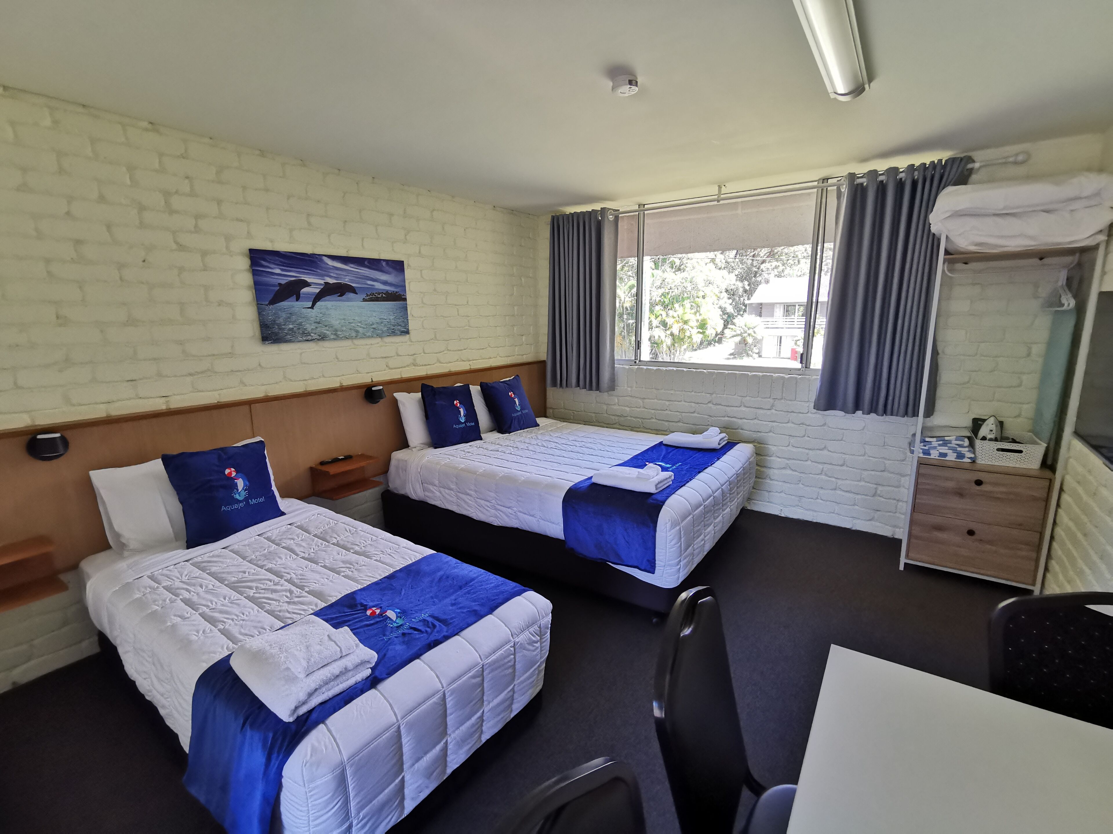 A hotel room with two beds, a desk, and a window with curtains.