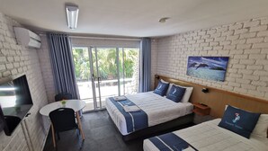Habitación de hotel con dos camas, un escritorio y un ventanal con vistas a palmeras.