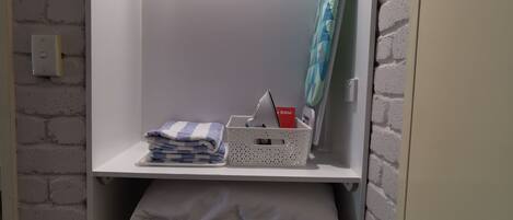 A closet with shelves containing folded clothes, a basket with a Bible, and a hanging rack with a towel.