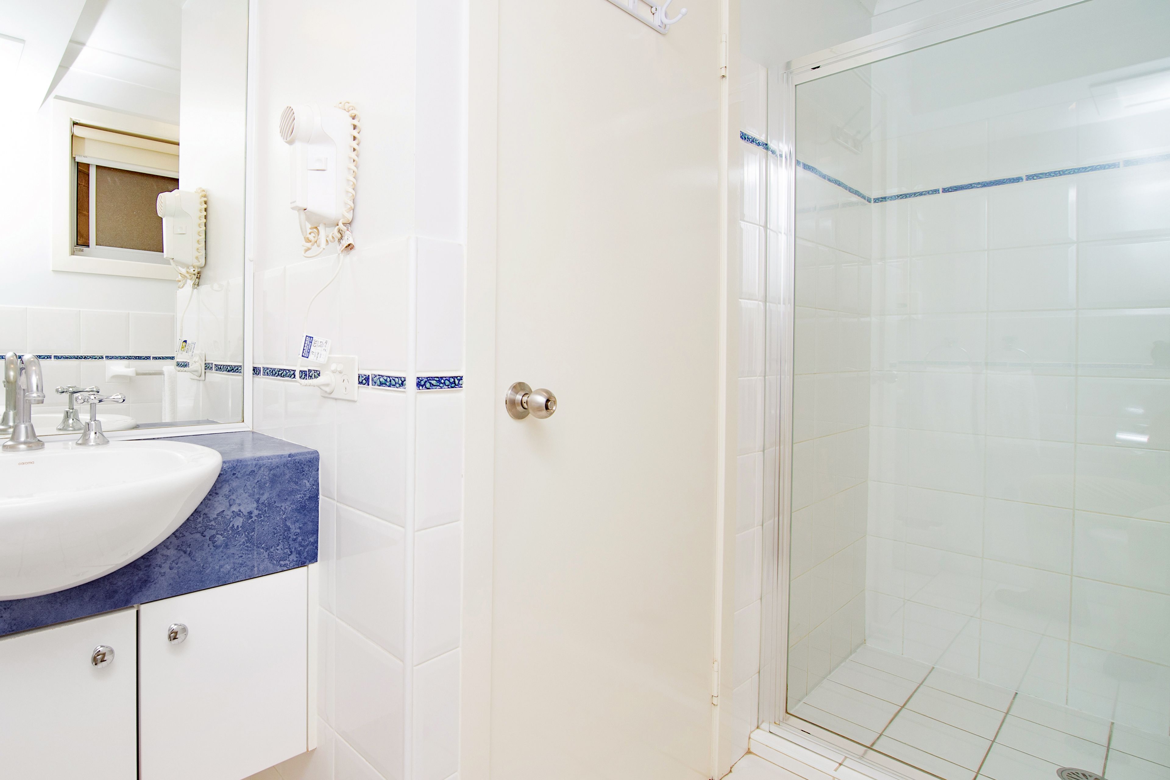 A bathroom with a white sink, blue countertop, and a glass shower enclosure.
