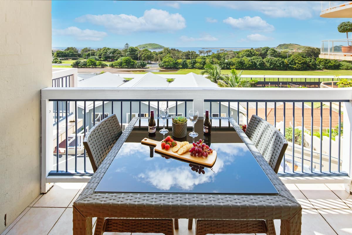 A balcony with a table set for a meal, featuring a bottle, wine glasses, and a fruit platter.