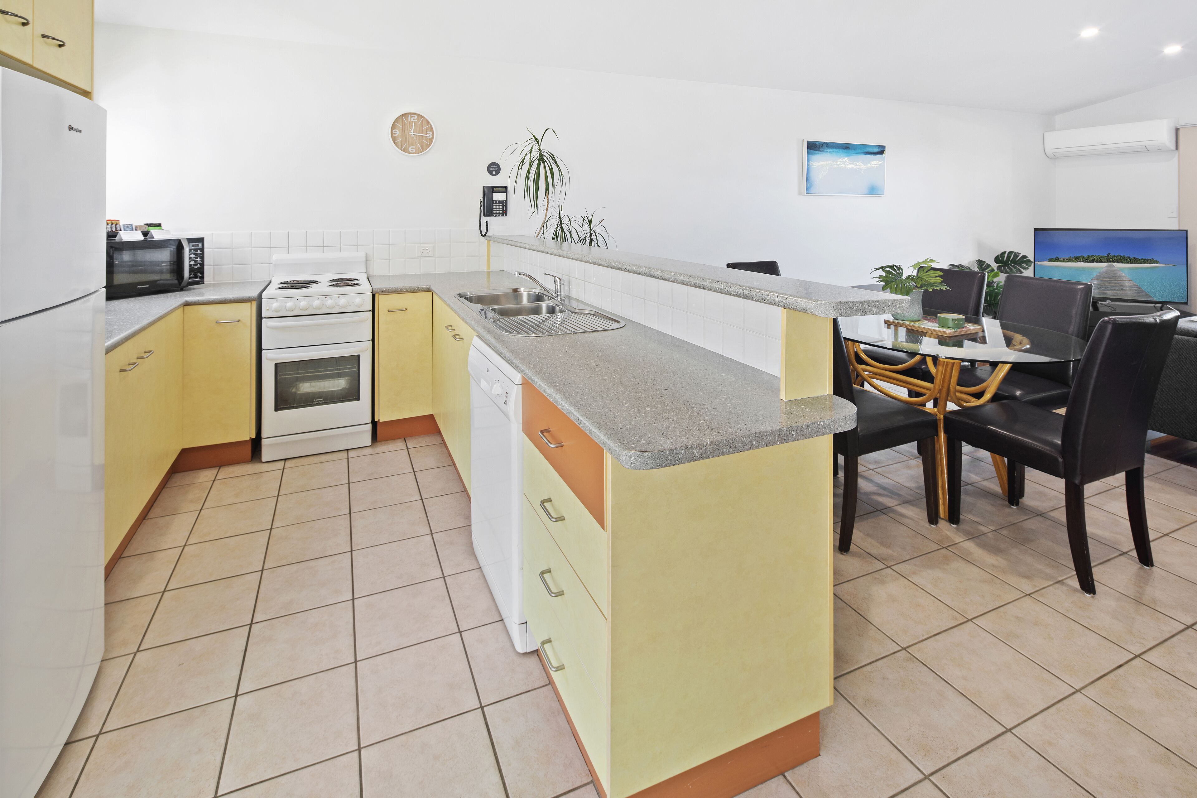 A compact kitchen with a dining area, featuring a microwave, stove, sink, and a small dining table with chairs.