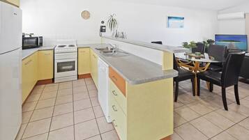 A compact kitchen with a dining area, featuring a microwave, stove, sink, and a small dining table with chairs.