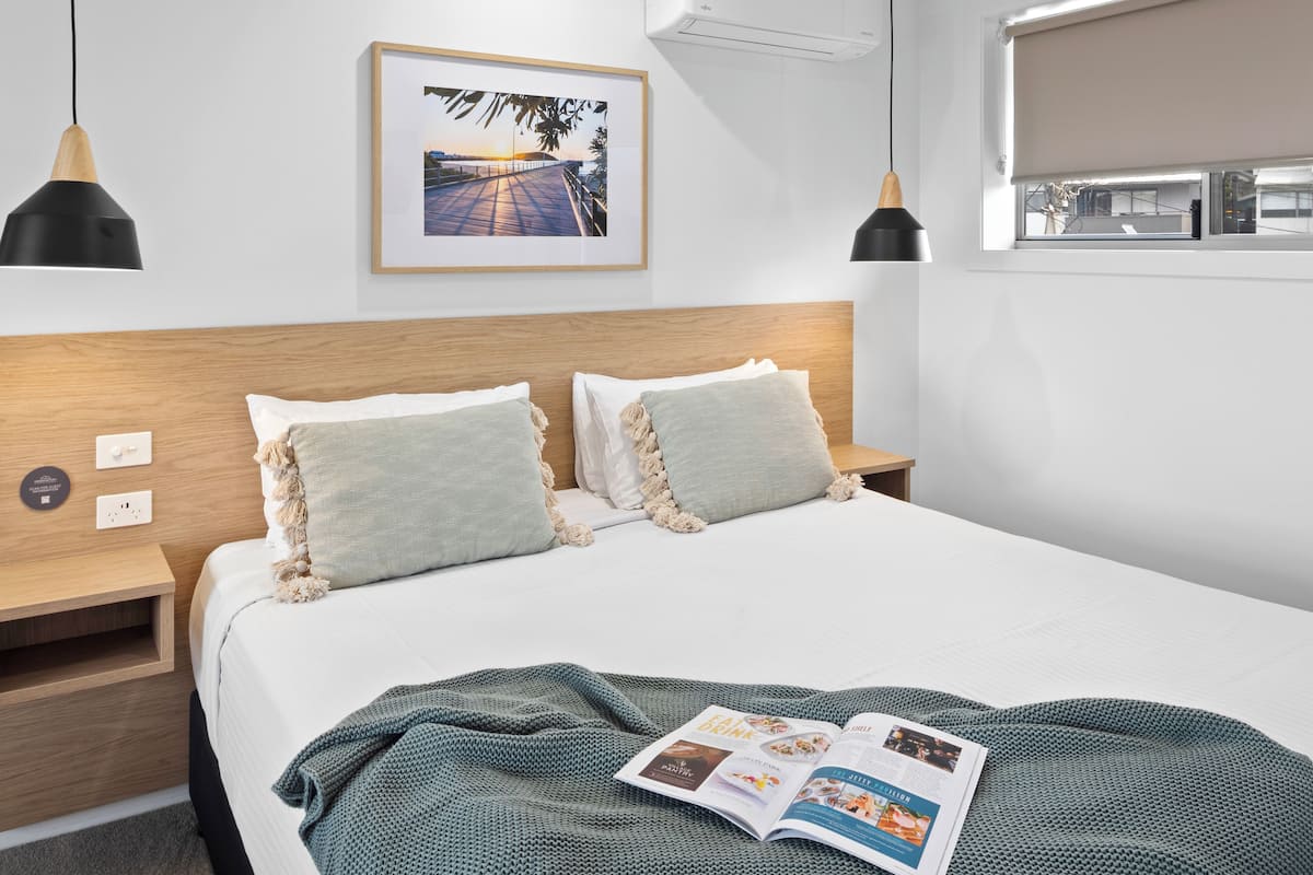 A neatly arranged hotel room with a large bed, two bedside tables, a framed picture on the wall, and a window with a view.