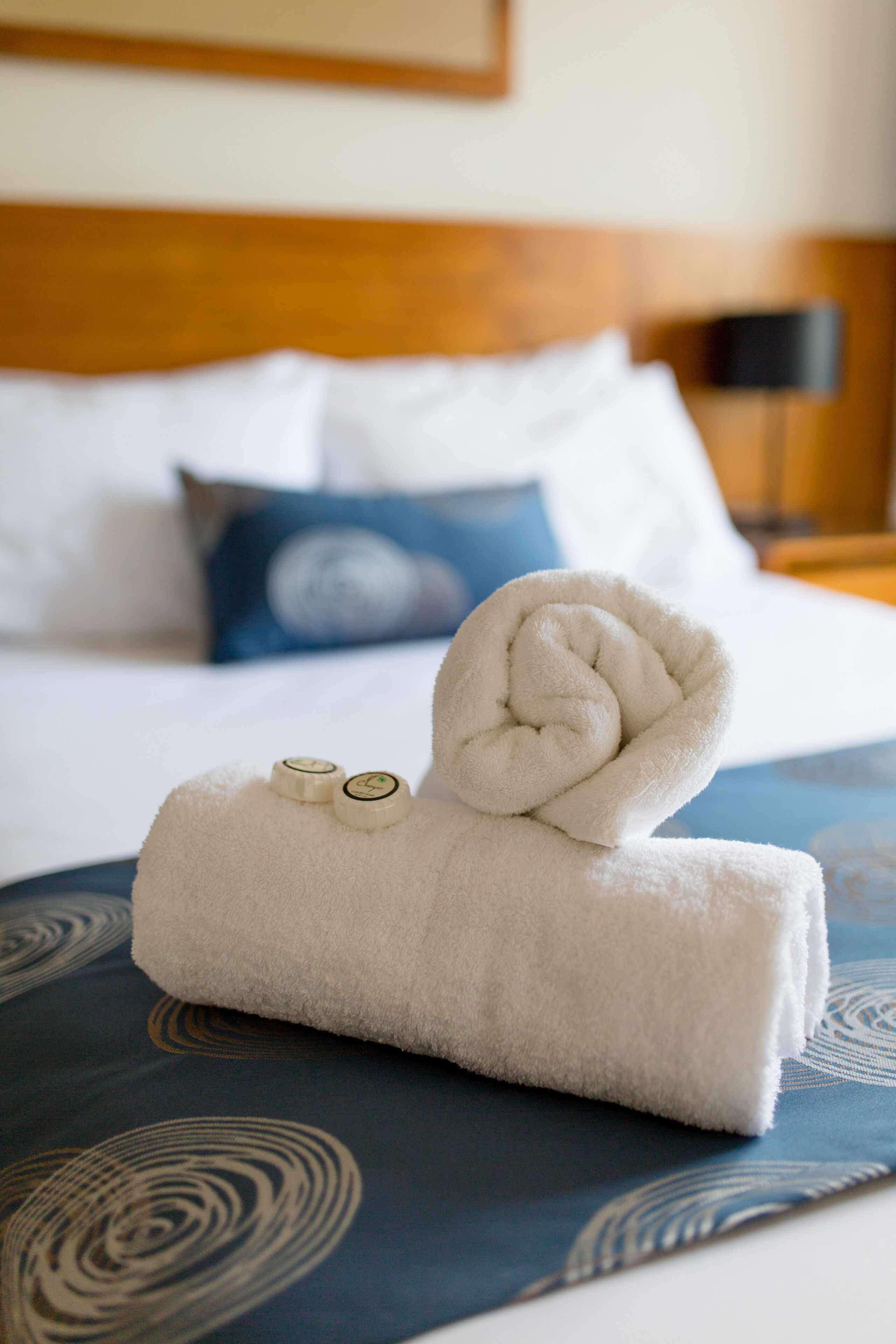 A neatly folded white towel with two circular objects on top, placed on a patterned blue bedspread.