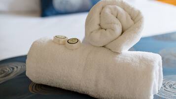 A neatly folded white towel with two circular objects on top, placed on a patterned blue bedspread.