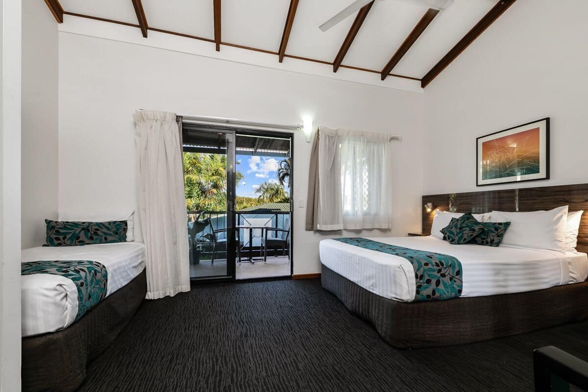 Habitación de hotel con dos camas, una puerta corrediza de vidrio a un patio y un ventilador de techo.