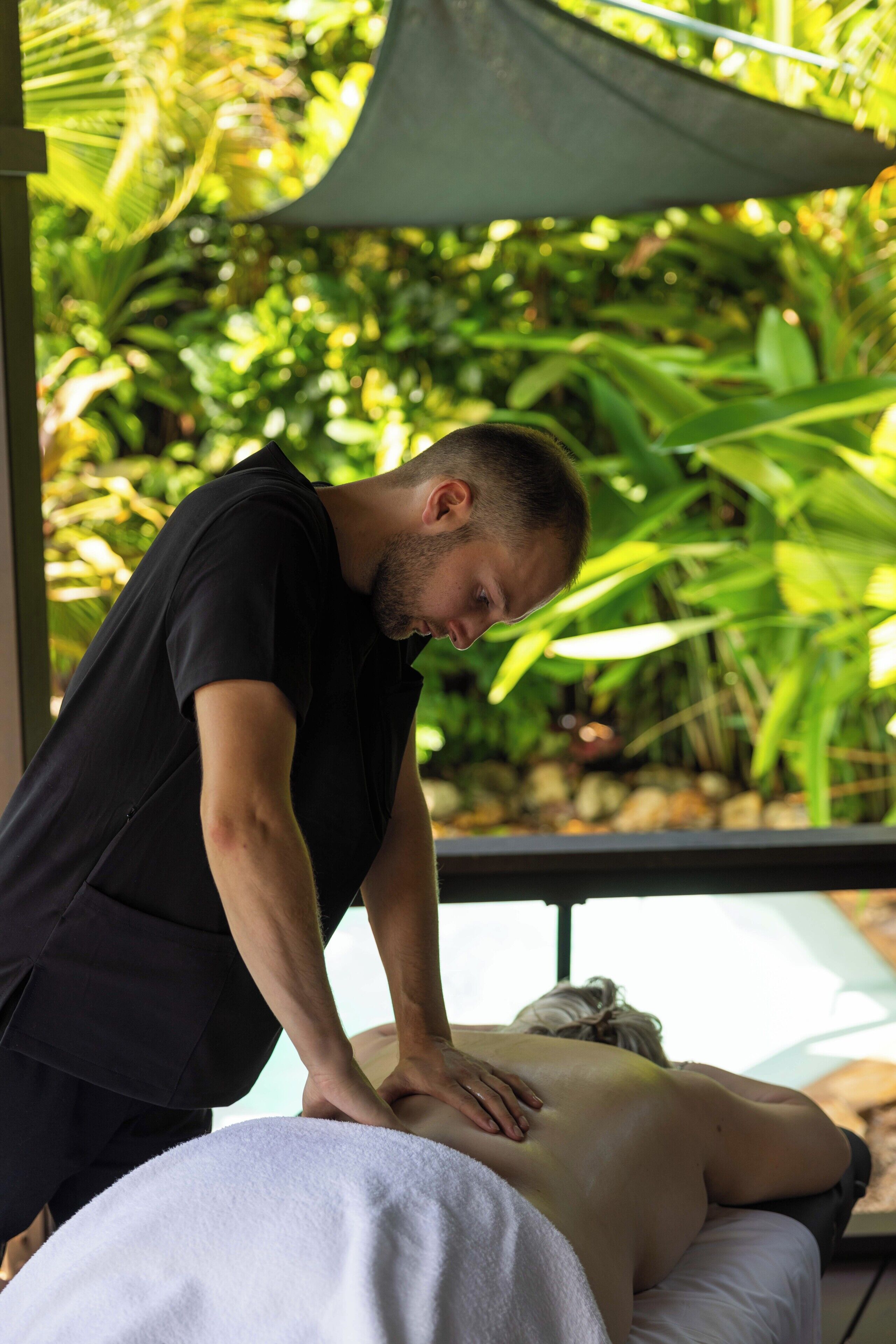 A person receiving a massage in a room with a view of lush greenery.