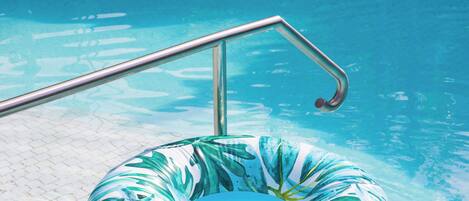 A swimming pool with a metal ladder and a leaf-patterned inflatable ring.