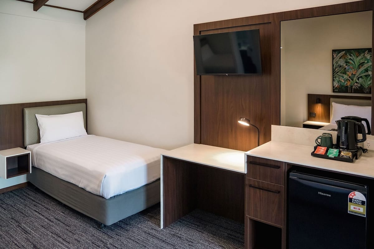 Habitación de hotel con cama, escritorio con cafetera, televisión y refrigerador pequeño.
