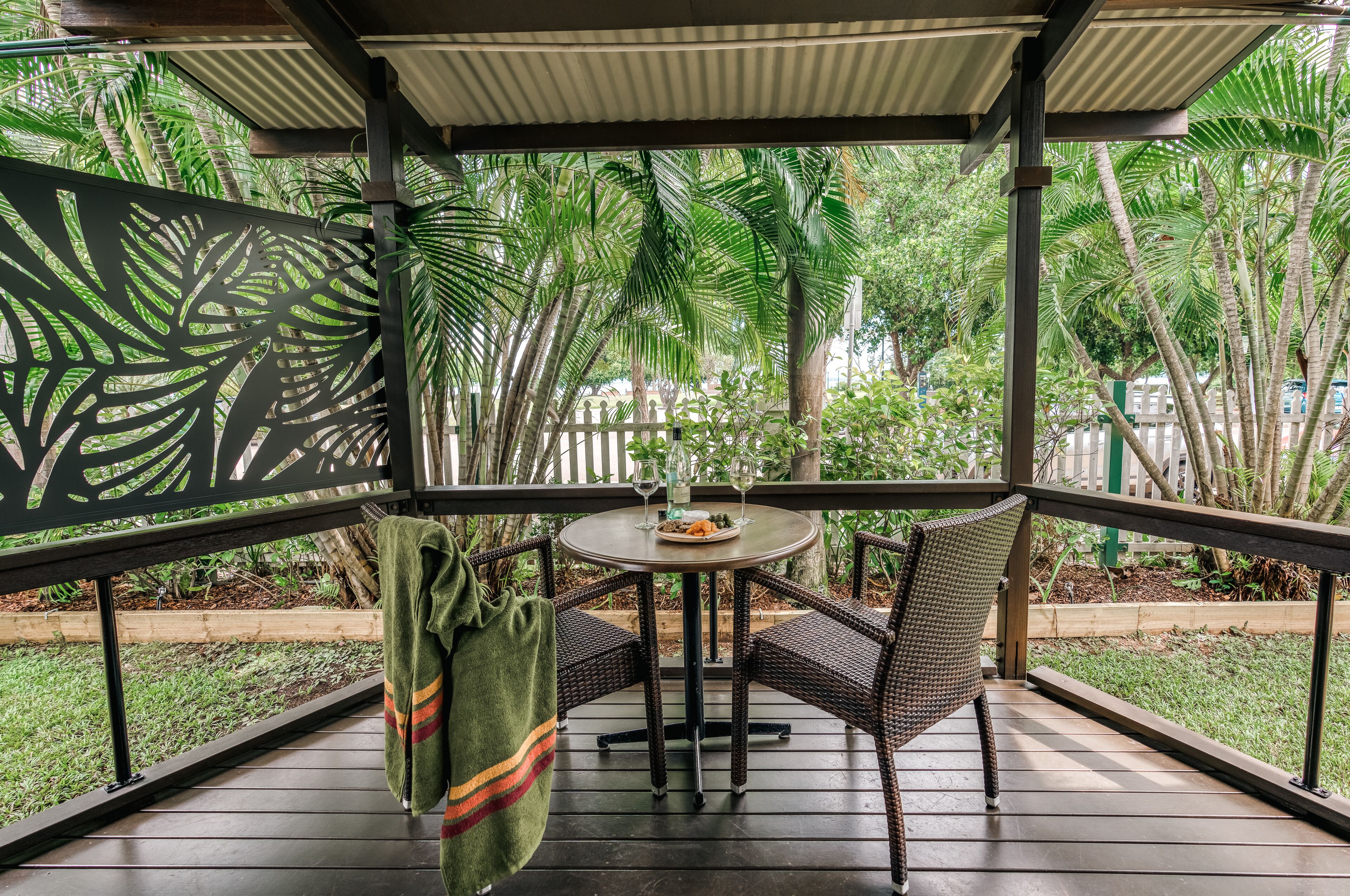 A covered outdoor patio with a round table and wicker chairs, surrounded by lush greenery.