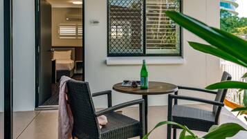 A balcony with wicker chairs, a table with a bottle and sunglasses, and a window with blinds.
