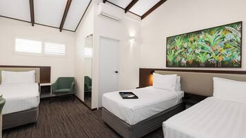 Habitación de hotel con dos camas, una silla verde, un cuadro en la pared y una puerta que da a otra habitación.